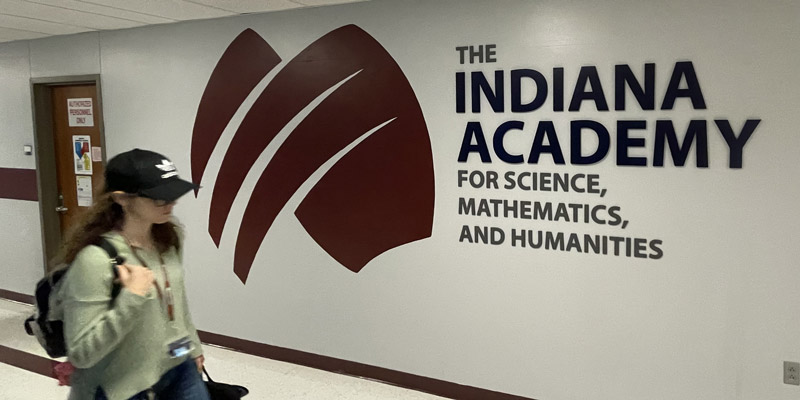 Student walking in hallway near Indiana Academy sign